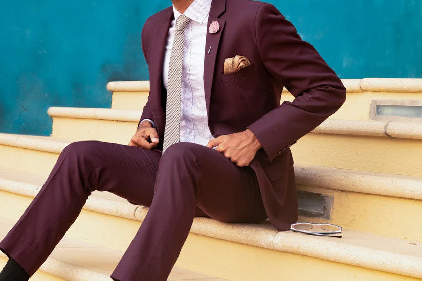 A man wearing maroon colored custom suit on stairs.