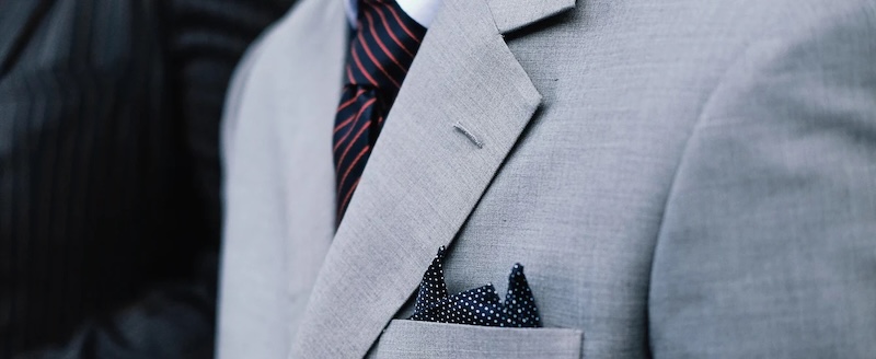 A close up of a gray suit with a red stripe tie, custom created by Pearce Bespoke.