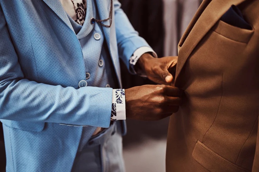 A close up of a man in a blue suit altering a brown bespoke suit - The Sustainability Edge: Incorporating Eco-Friendly Practices