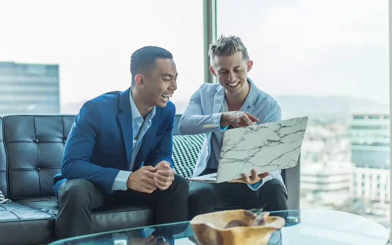 Two men in bespoke suits sitting on a couch in front of a computer - learn how to embrace technology in your franchise with Pearce Bespoke.